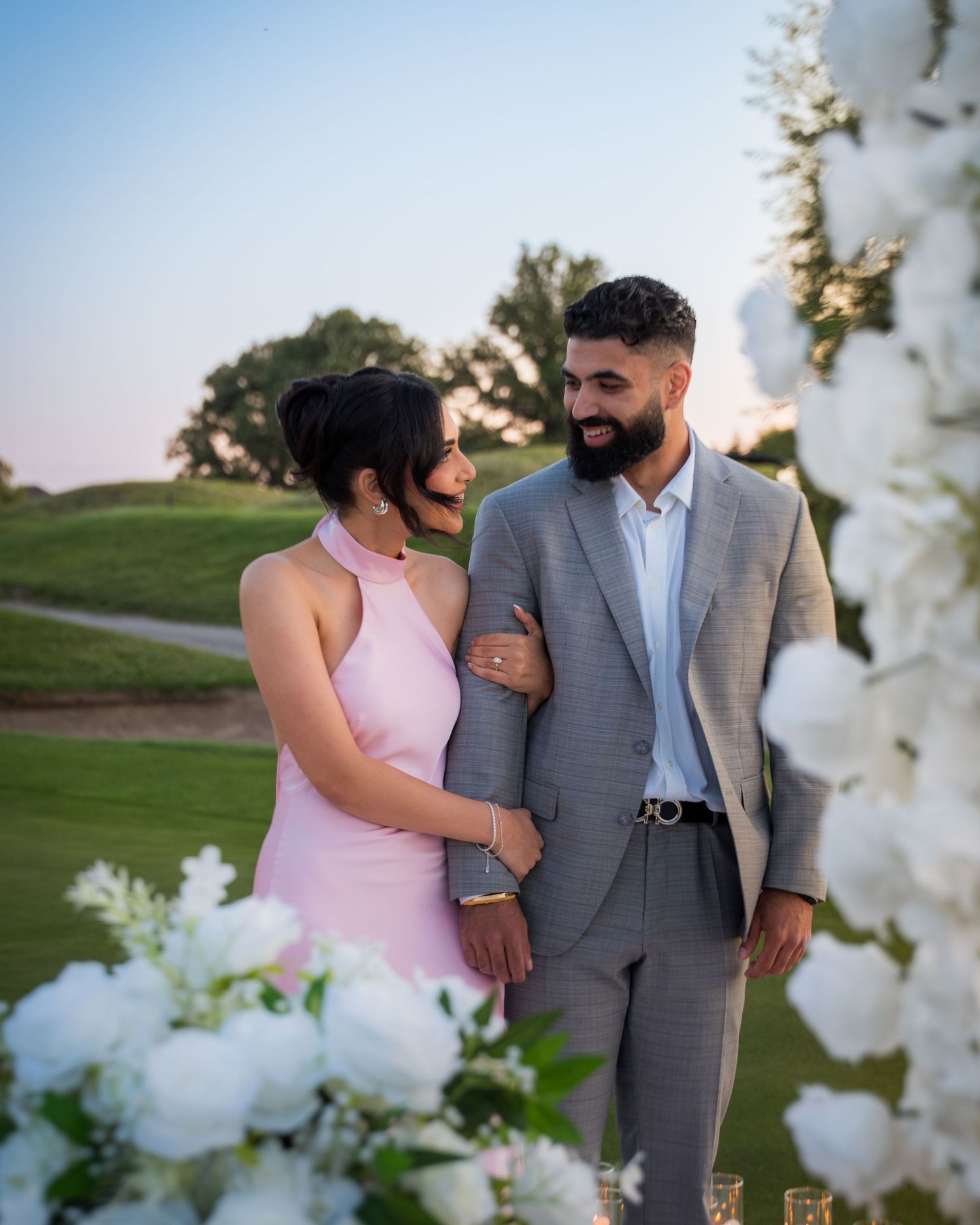 Couple shares laughs during sunset photography session with white floral arch.