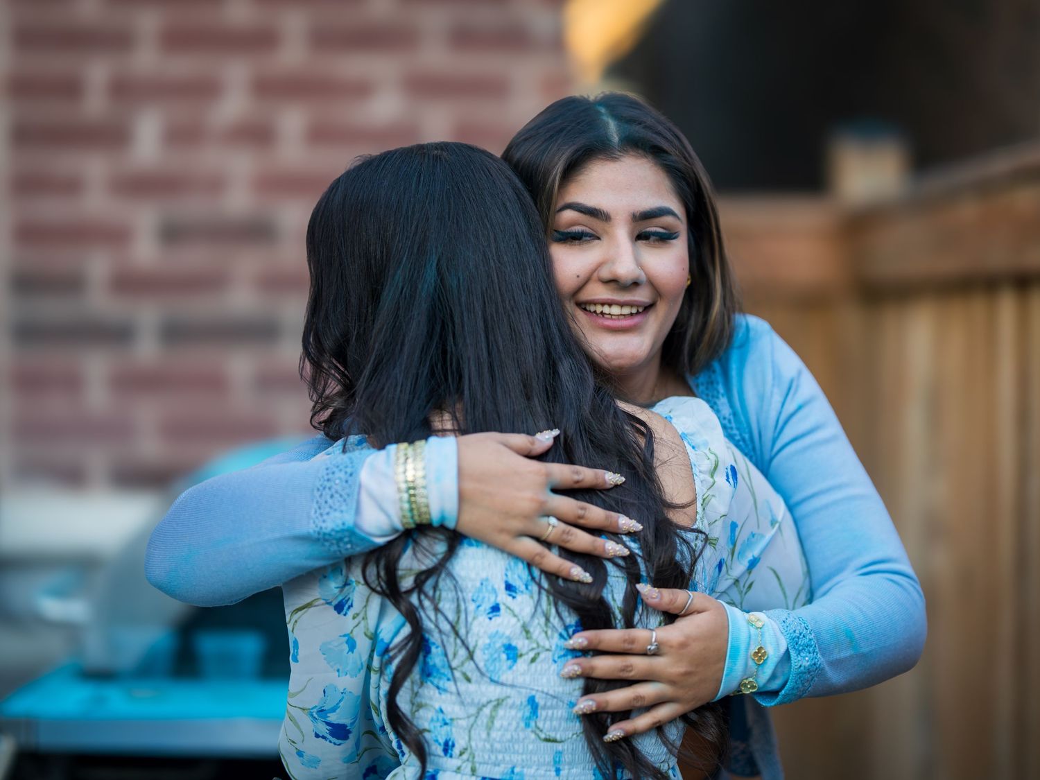 Two women sharing a warm embrace and smiling at an outdoor backyard celebration party.