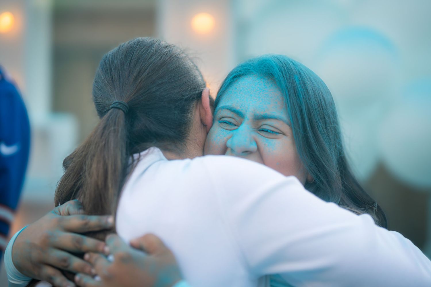 Two women sharing a warm hug, one with blue powder on her face at a gender reveal party.