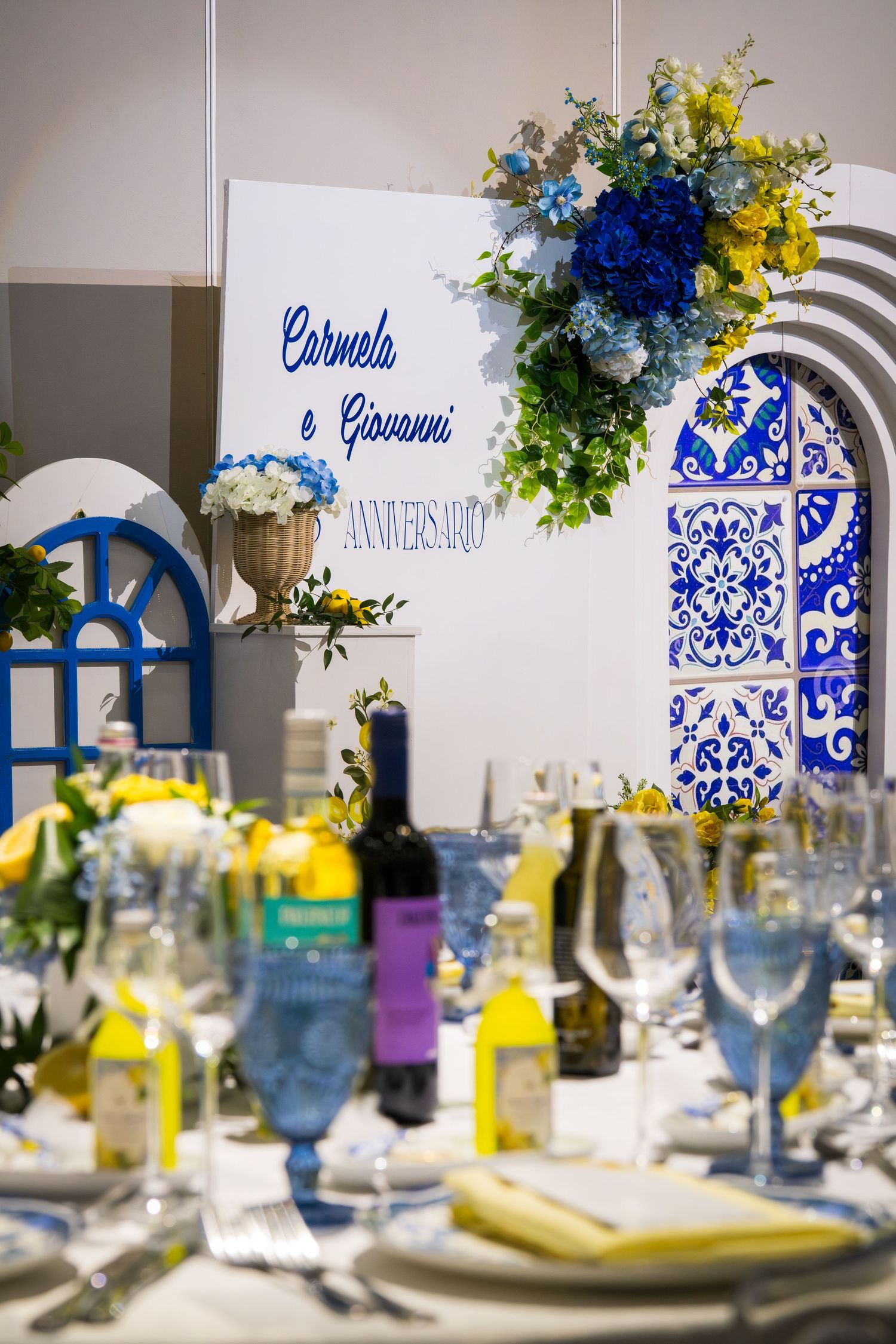 Elegant anniversary table setting for Carmela e Giovanni with blue and yellow floral decor and Mediterranean-inspired backdrop.