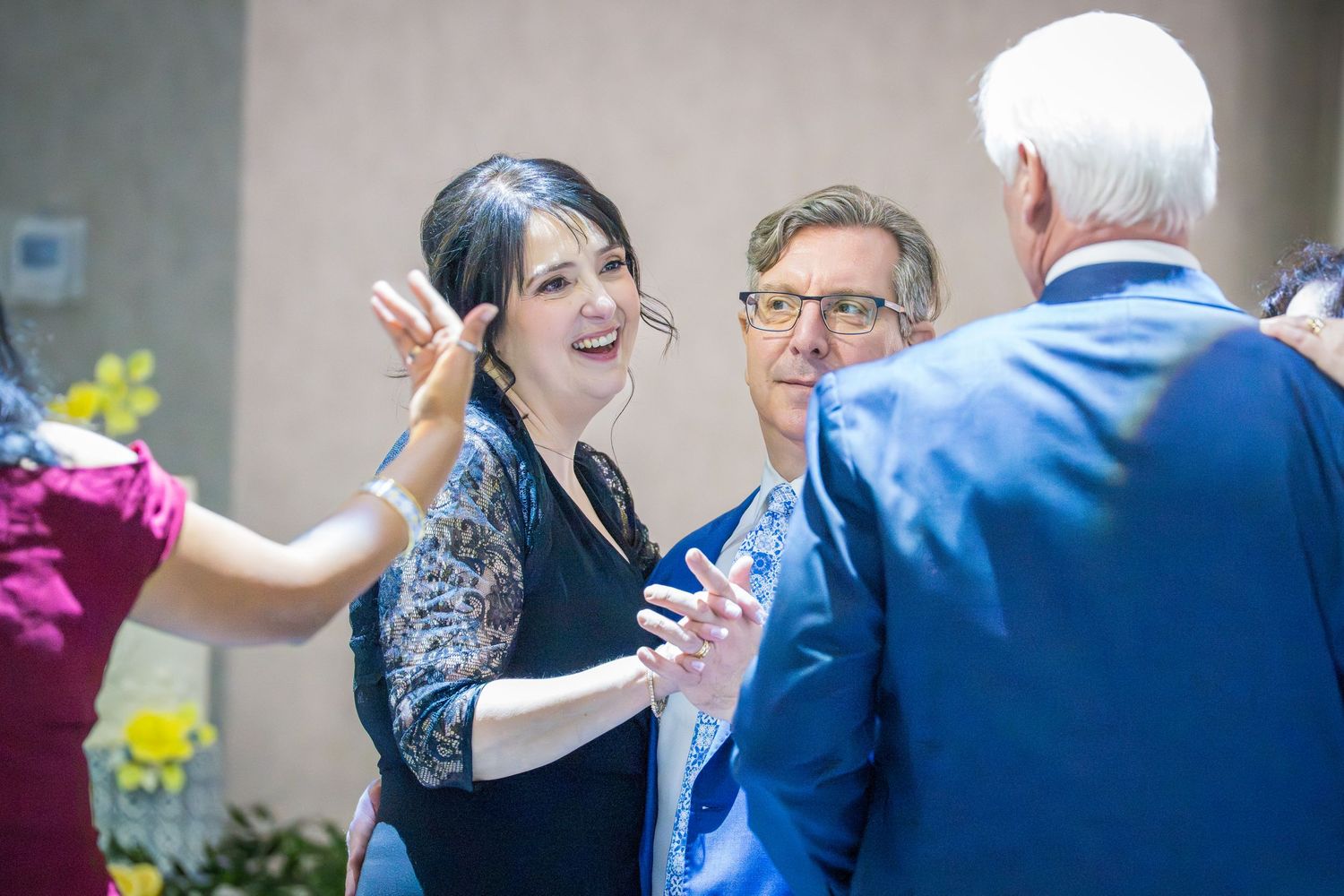 Woman gesturing while conversing with two men in blue suits at a wedding reception.