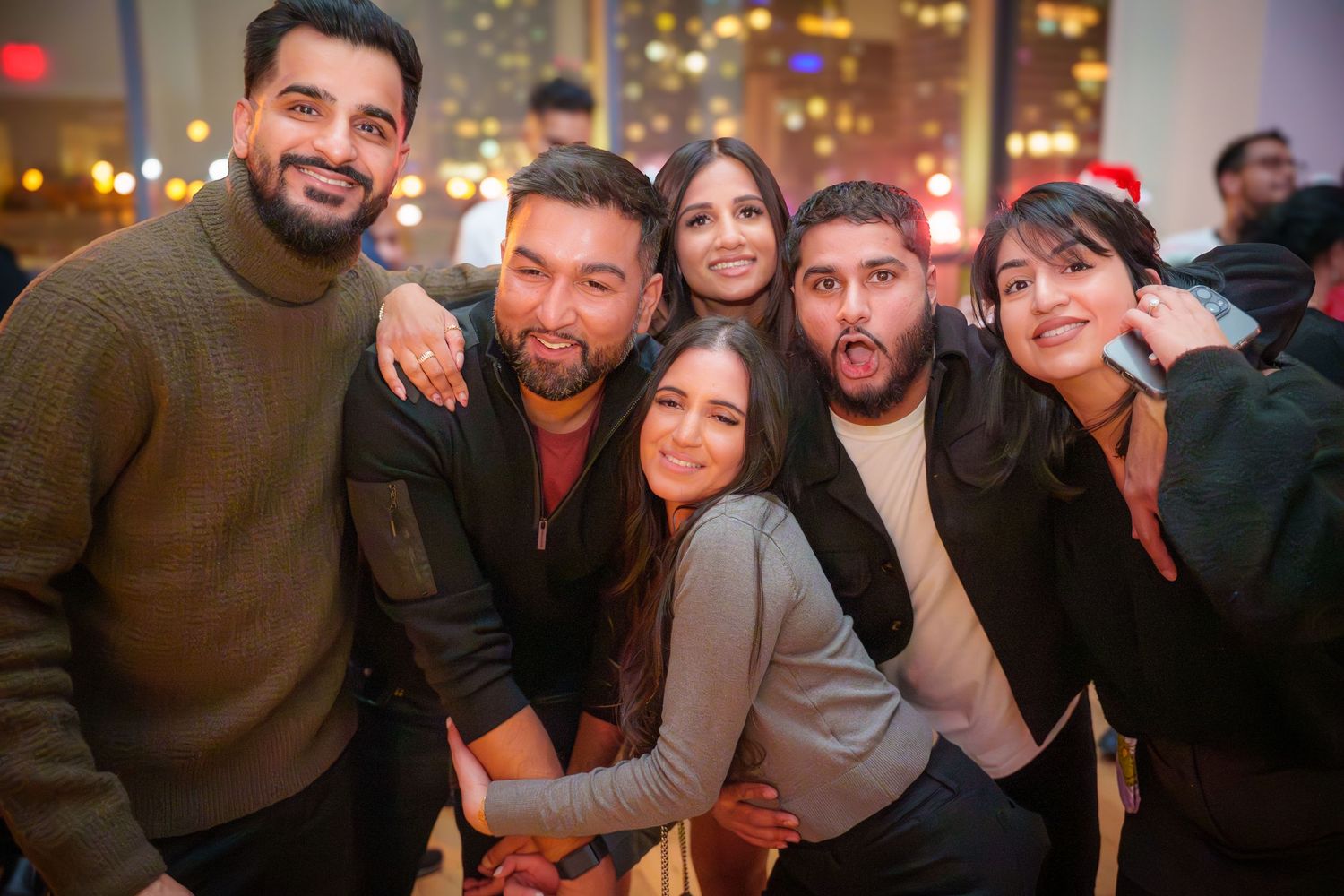 Friends gathered together at a nighttime indoor celebration with festive lighting.