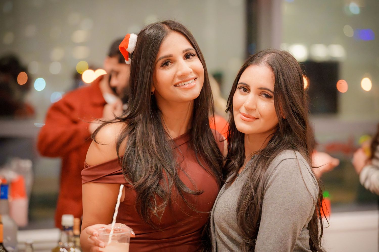 Two people in festive attire smile together at an evening event with blurred lights in background.