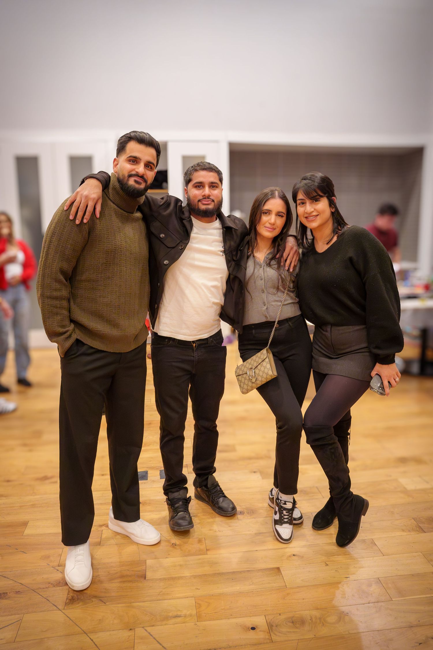 Friends pose together at a casual indoor party with wooden flooring.