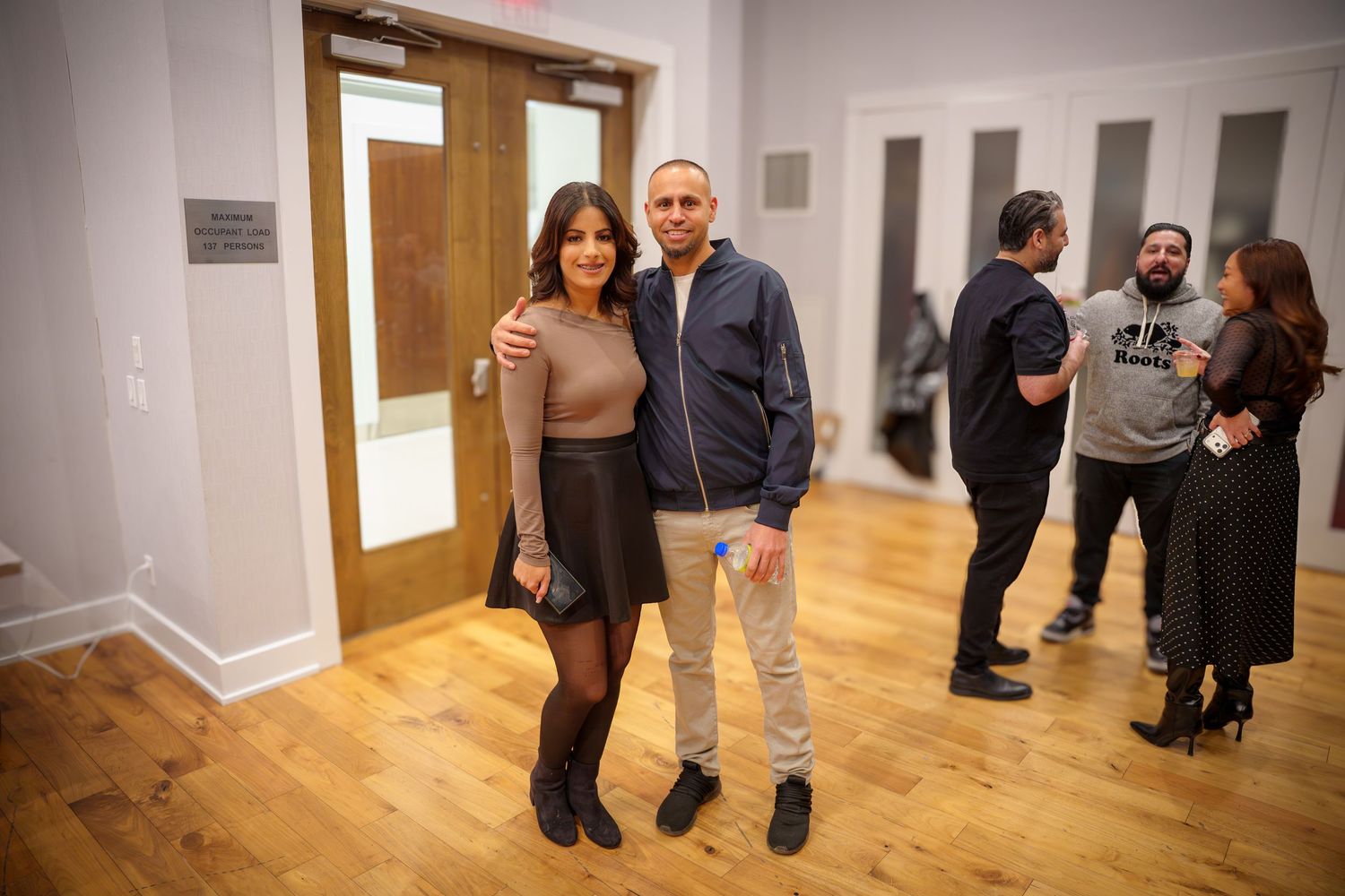 People gather in a bright gallery space with wooden floors and white walls for an exhibition or event.