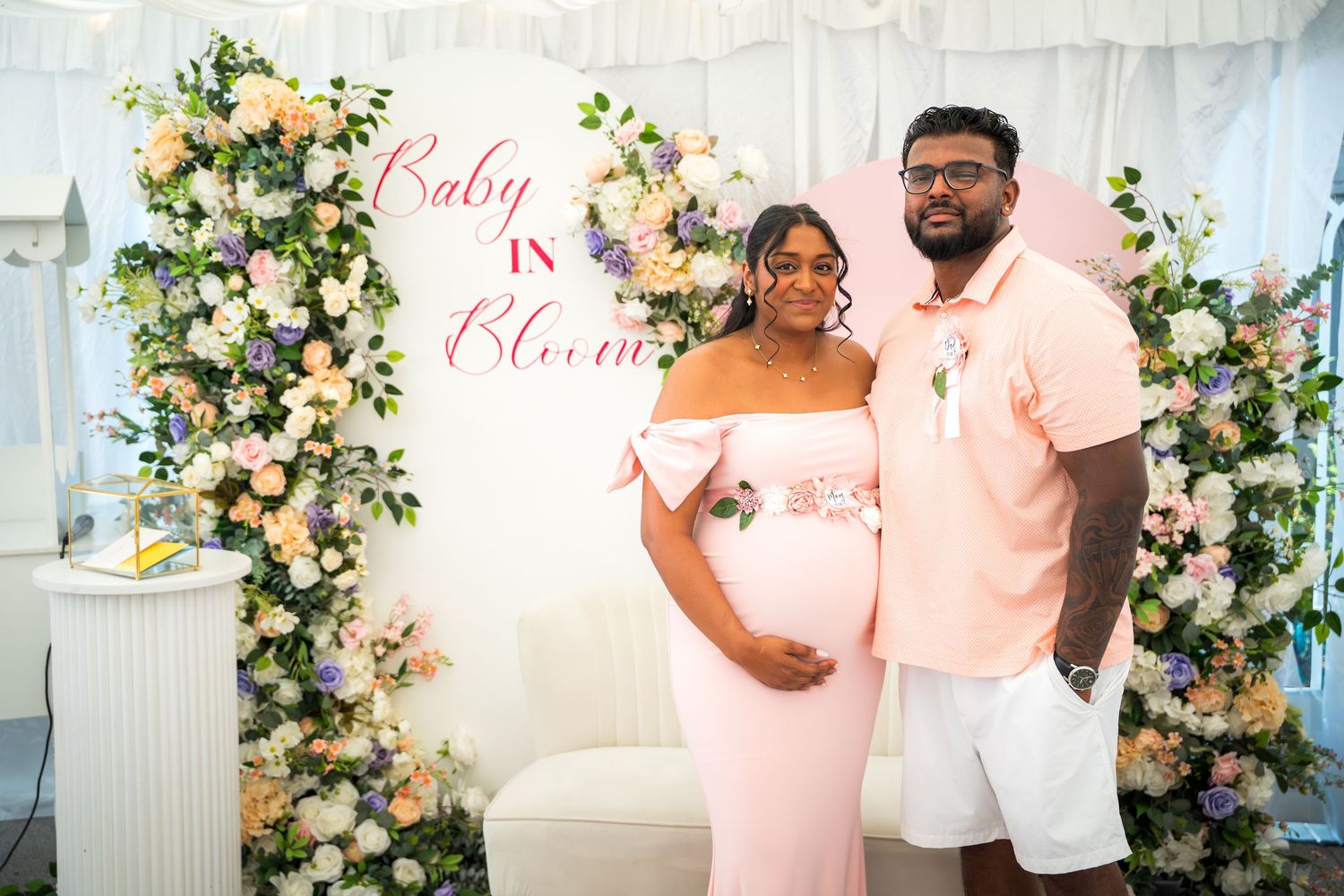 Baby shower celebration with pink and white decor featuring floral arrangements and elegant backdrop.