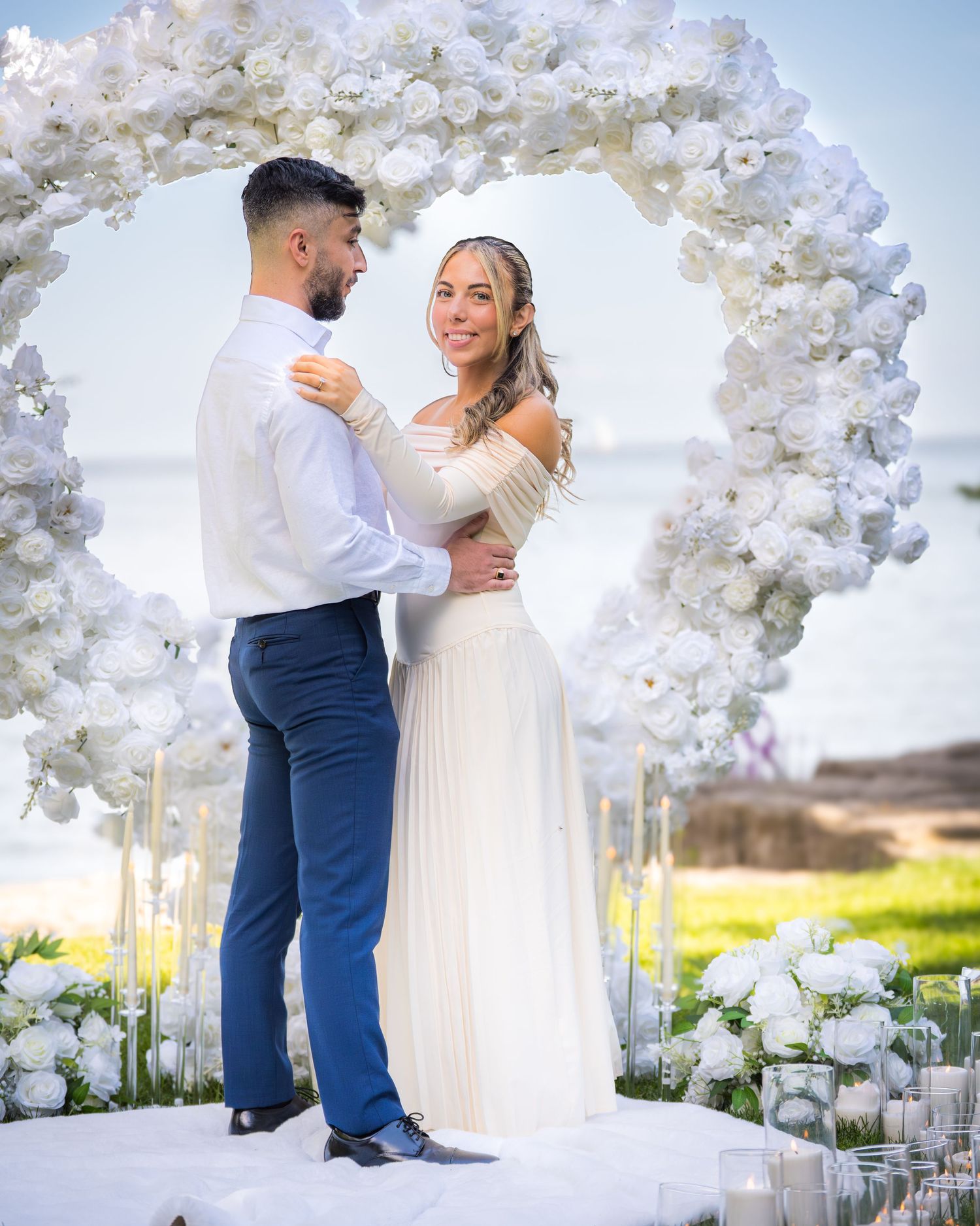 Beautiful oceanfront wedding setup with white floral archway and candlelit path on grassy cliff.