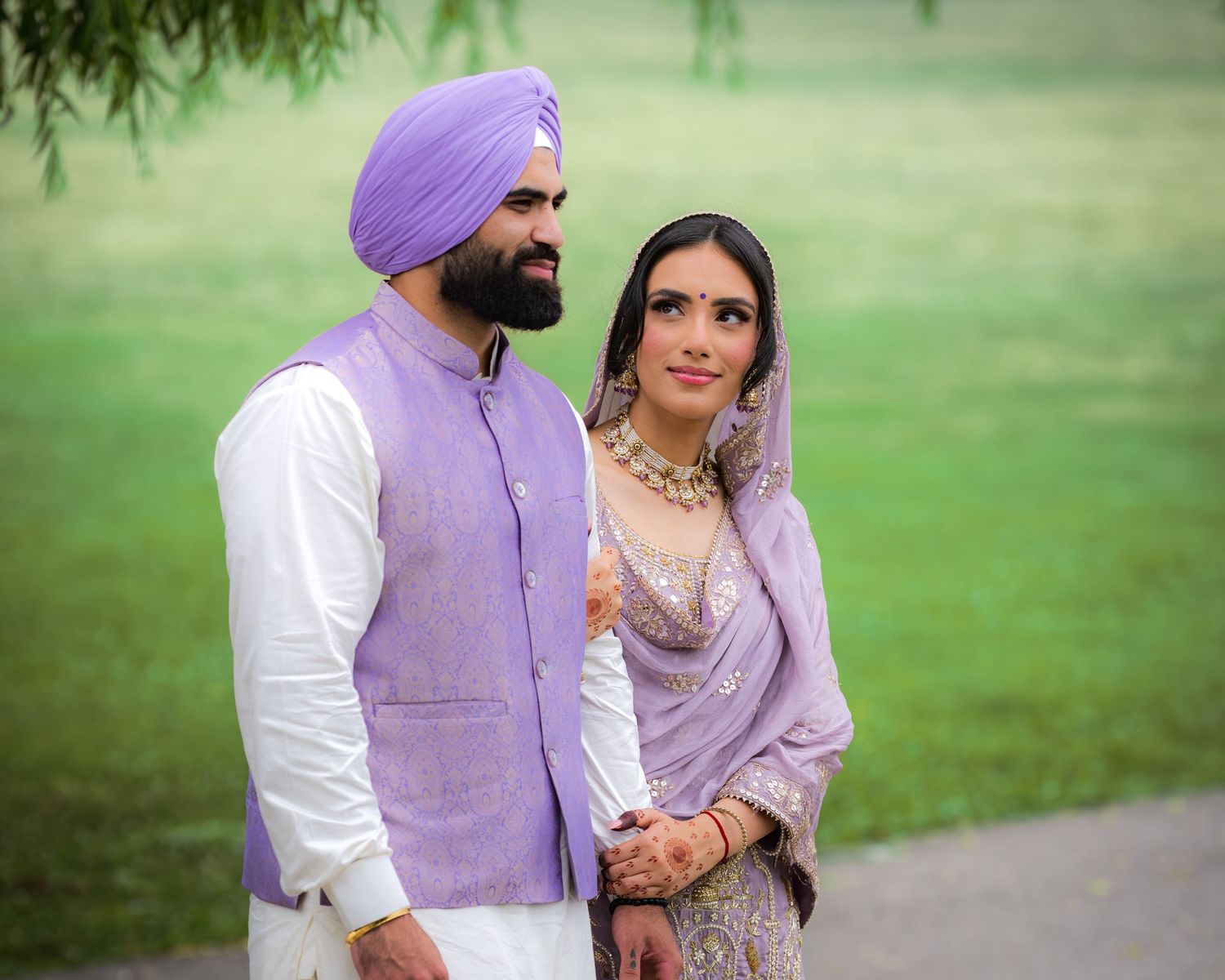 A couple in coordinated purple and white traditional Indian attire posing in a garden setting.