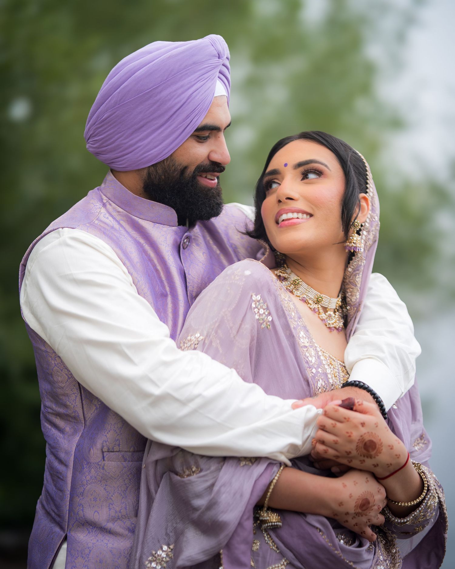 Couple in coordinated purple and white outfits share loving glances outdoors.