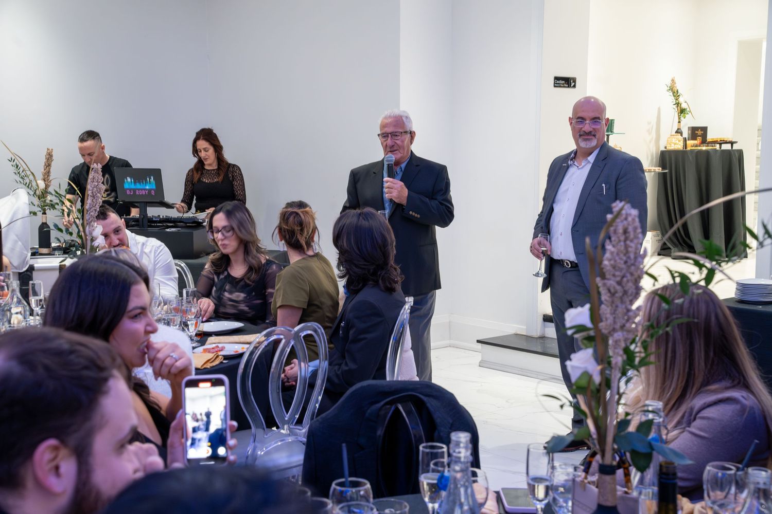 Professional gathering in a modern white venue with guests seated at multiple tables.