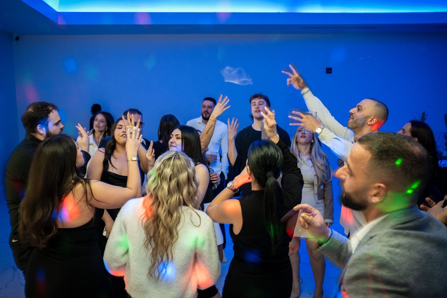 Guests dancing enthusiastically with hands in the air at a party with blue lighting effects.