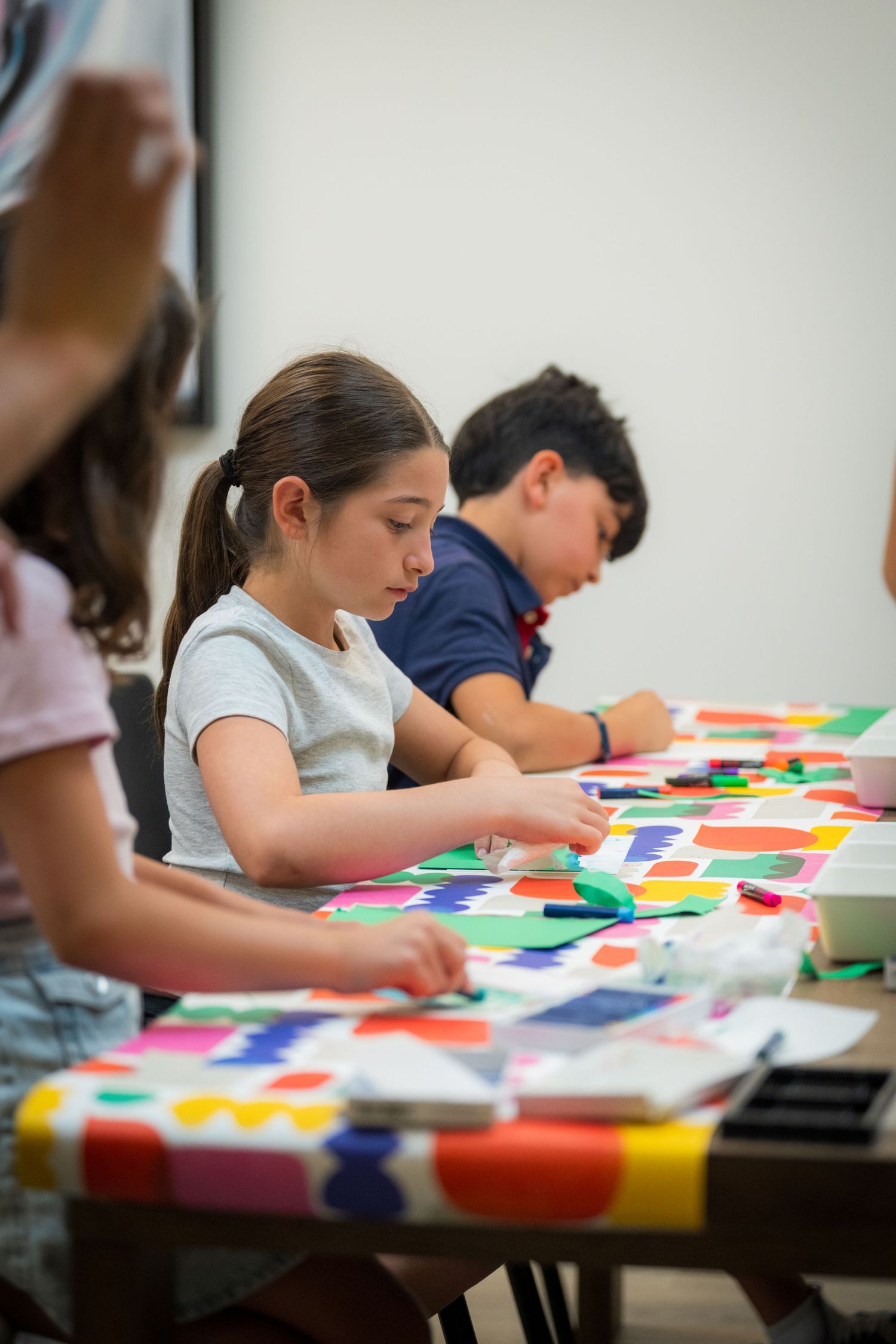 Children work on colorful paper collage art projects at a vibrant craft table.