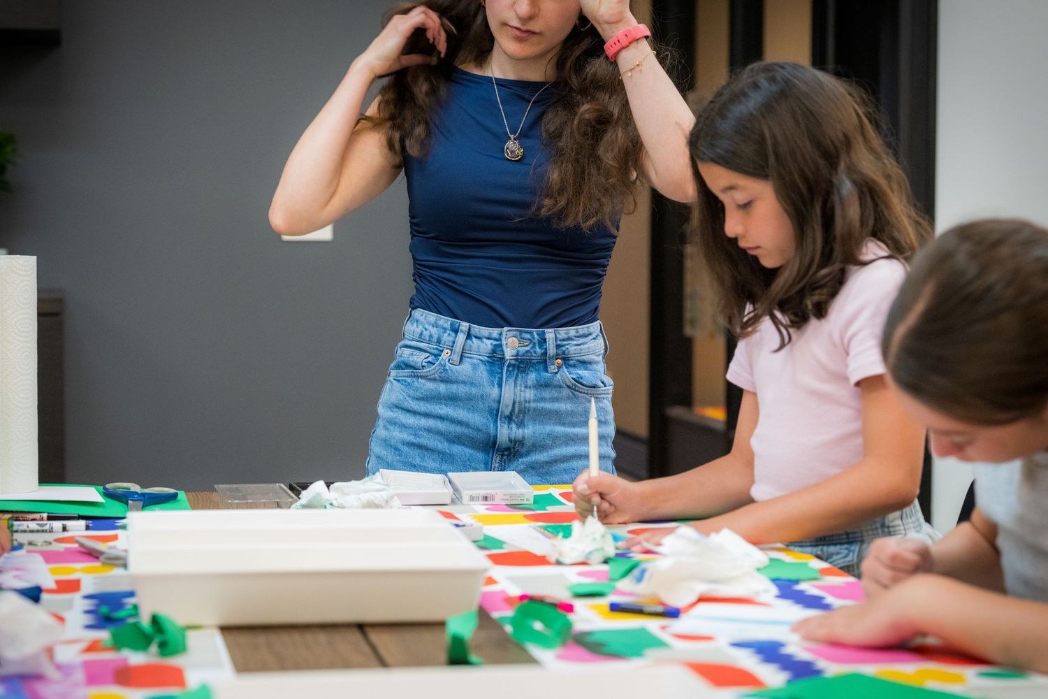 Art teacher supervises children working on vibrant paper collage craft projects.