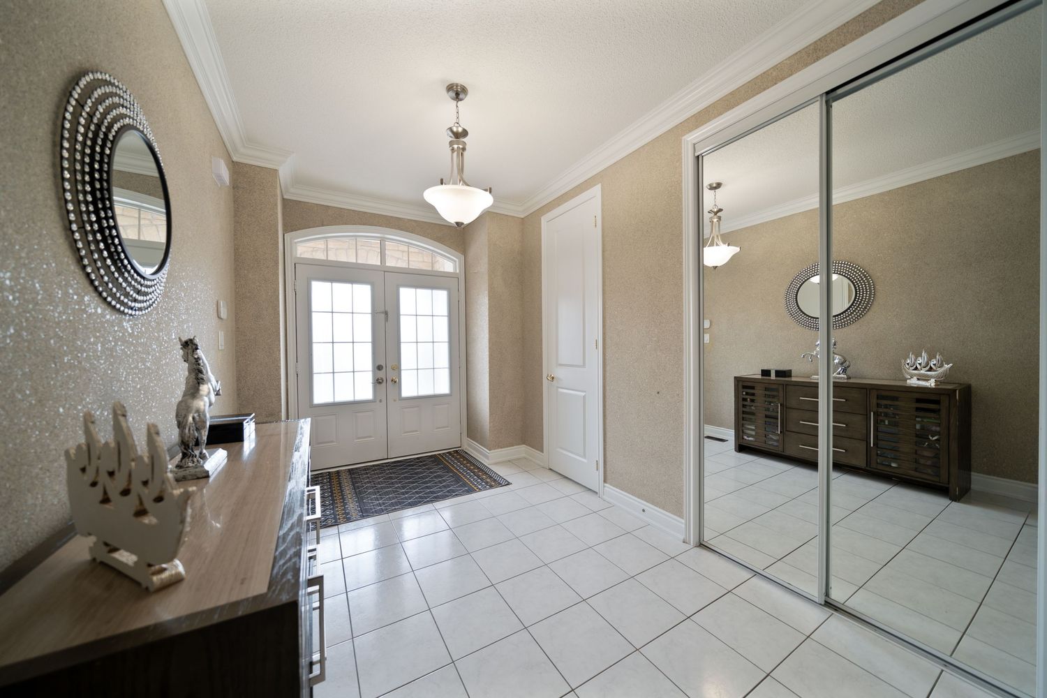 Modern interior hallway with tile flooring, beige walls, and natural lighting from windows and glass doors.