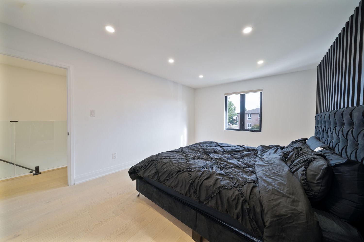 Modern minimalist bedroom with black bedding, white walls, and recessed lighting creates a sleek contemporary space.