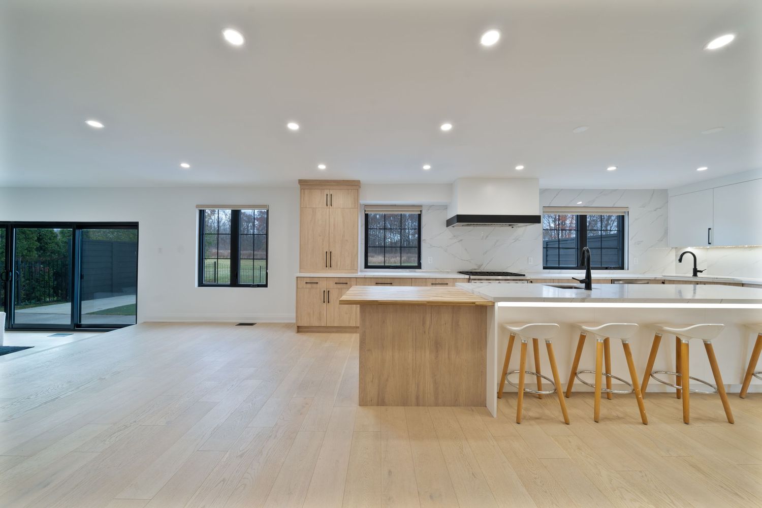 Modern open concept kitchen and living space with recessed lighting and light wood cabinetry showcases a minimalist design.