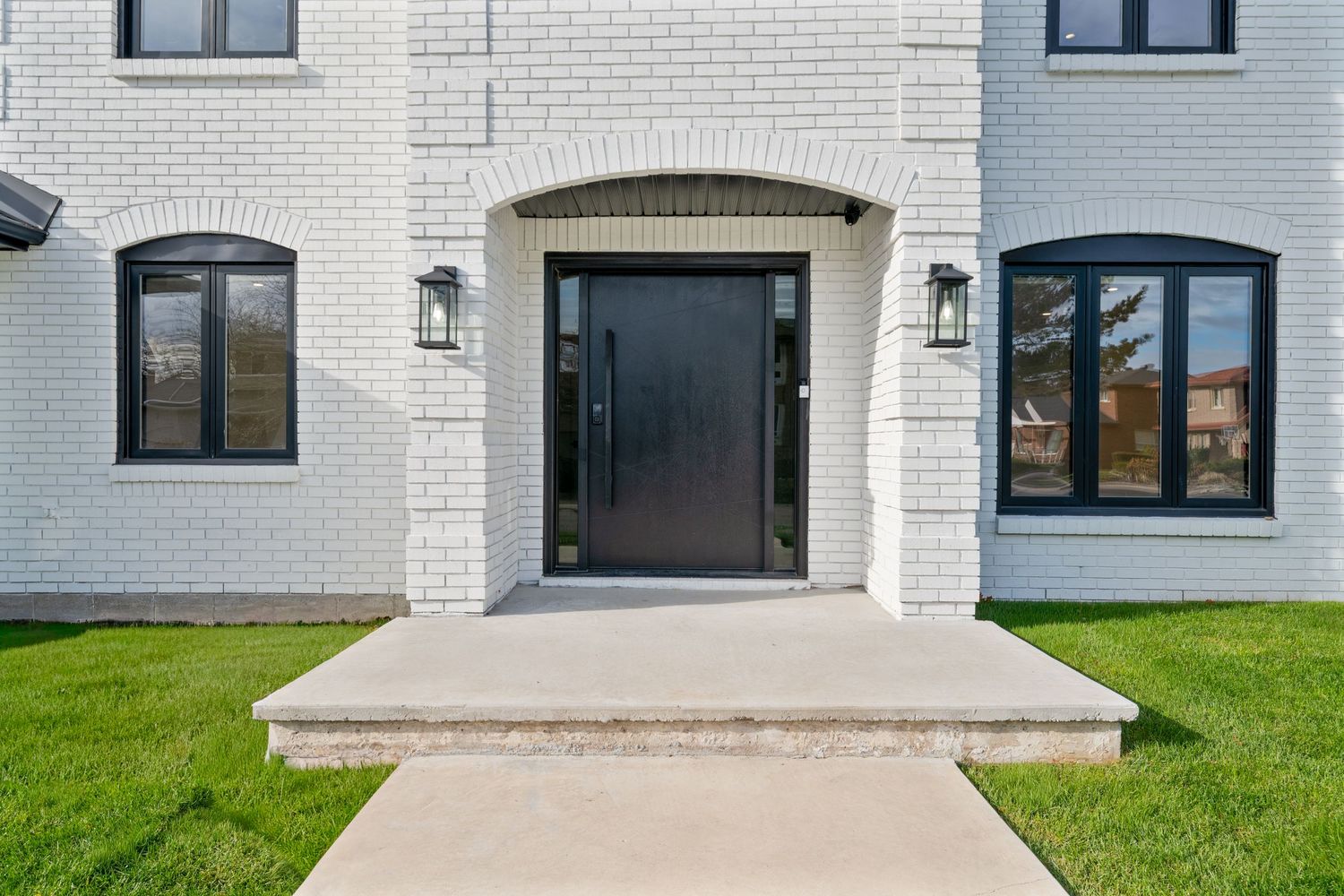 Modern white brick house exterior with black-framed windows and arched architectural details against green lawn.