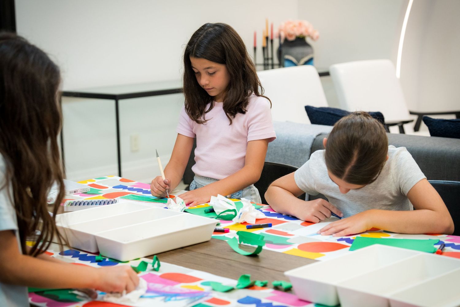 Three children collaborate on a colorful paper collage art project at a table.