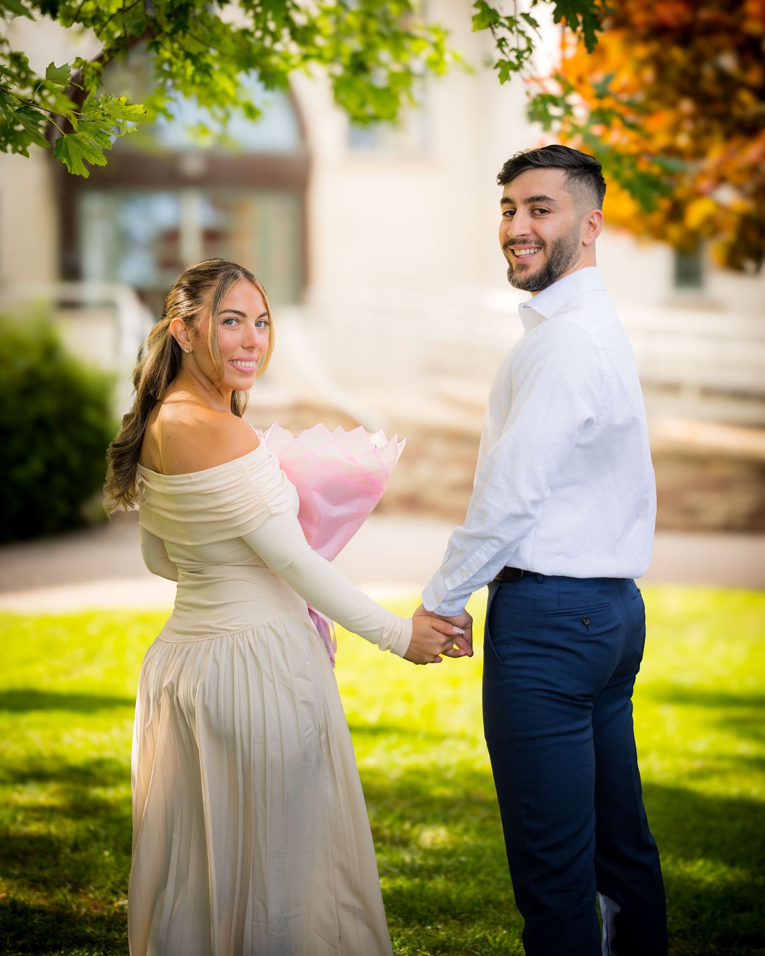 A couple in formal attire share a romantic dance moment together in a sunlit garden setting with autumn foliage.