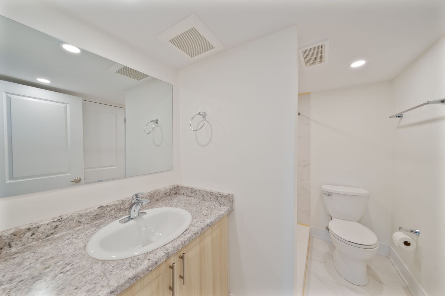 Modern bathroom interior with white vanity, granite countertop, and recessed lighting in a clean, minimalist design.