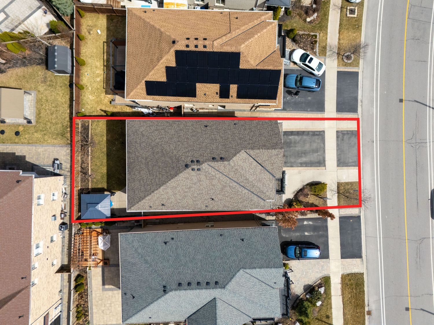 Aerial drone view of residential properties with gray rooftops and driveways bordered by red property lines.