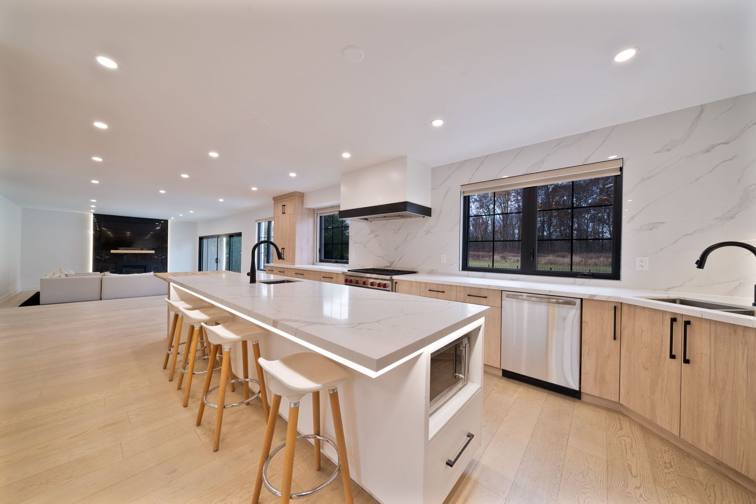 Modern open concept kitchen and dining area with light wood floors and white cabinets in a bright minimalist space.