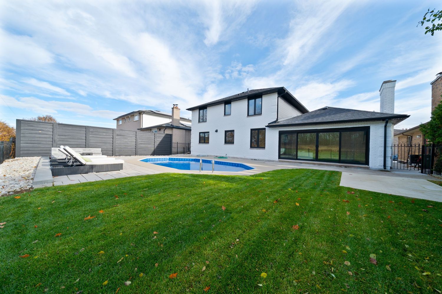 A panoramic view of a modern house exterior with a sloping green lawn and white trim against a blue sky.