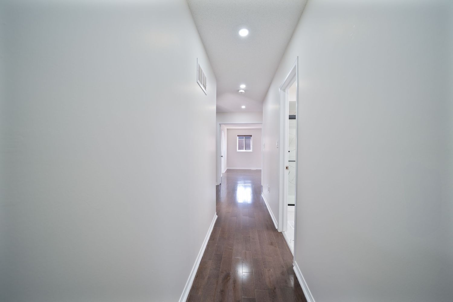 Long empty hallway with white walls, fluorescent lighting, and doors leading to various rooms.