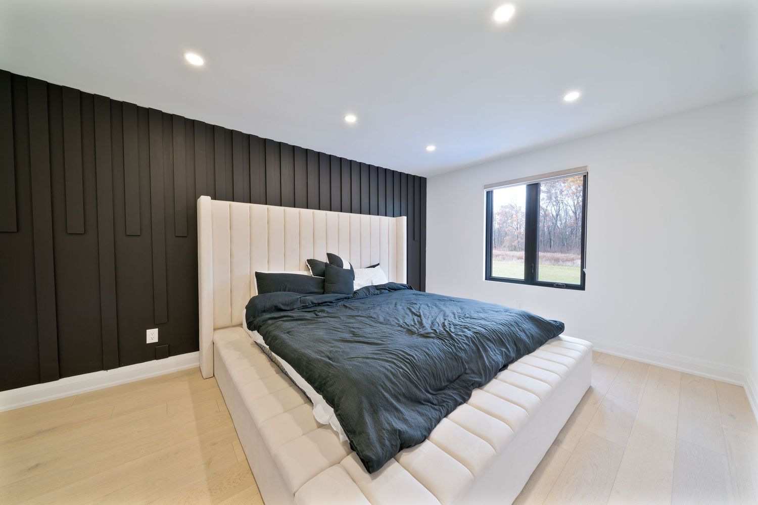 Modern bedroom interior with dark accent wall, recessed lighting, and grey bedding in minimalist design.