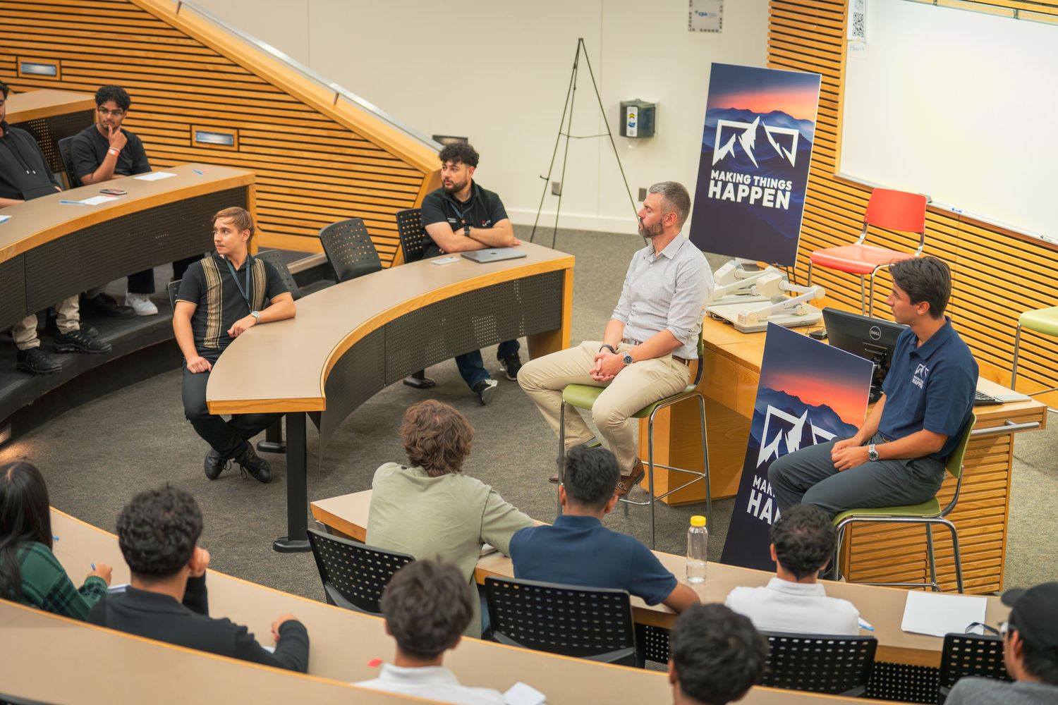 Conference room meeting with multiple attendees seated in front of wooden slatted walls.