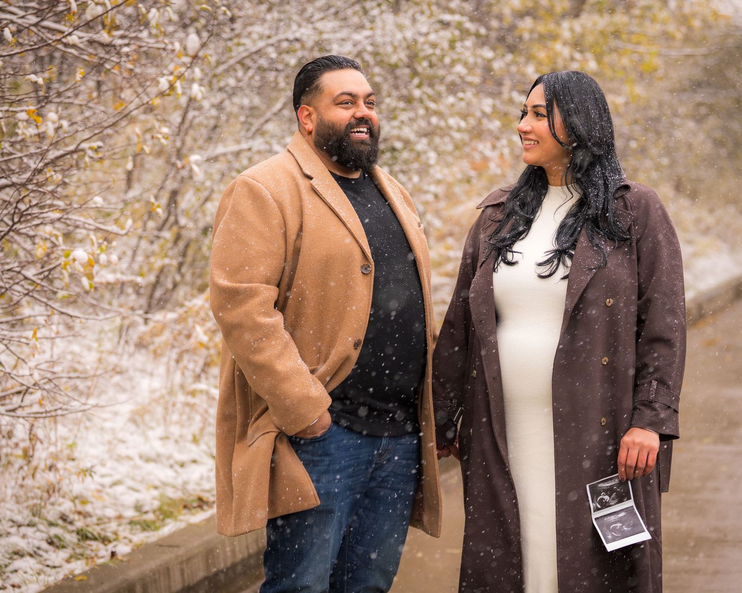 Couple in winter coats standing together during snowy weather outdoors.