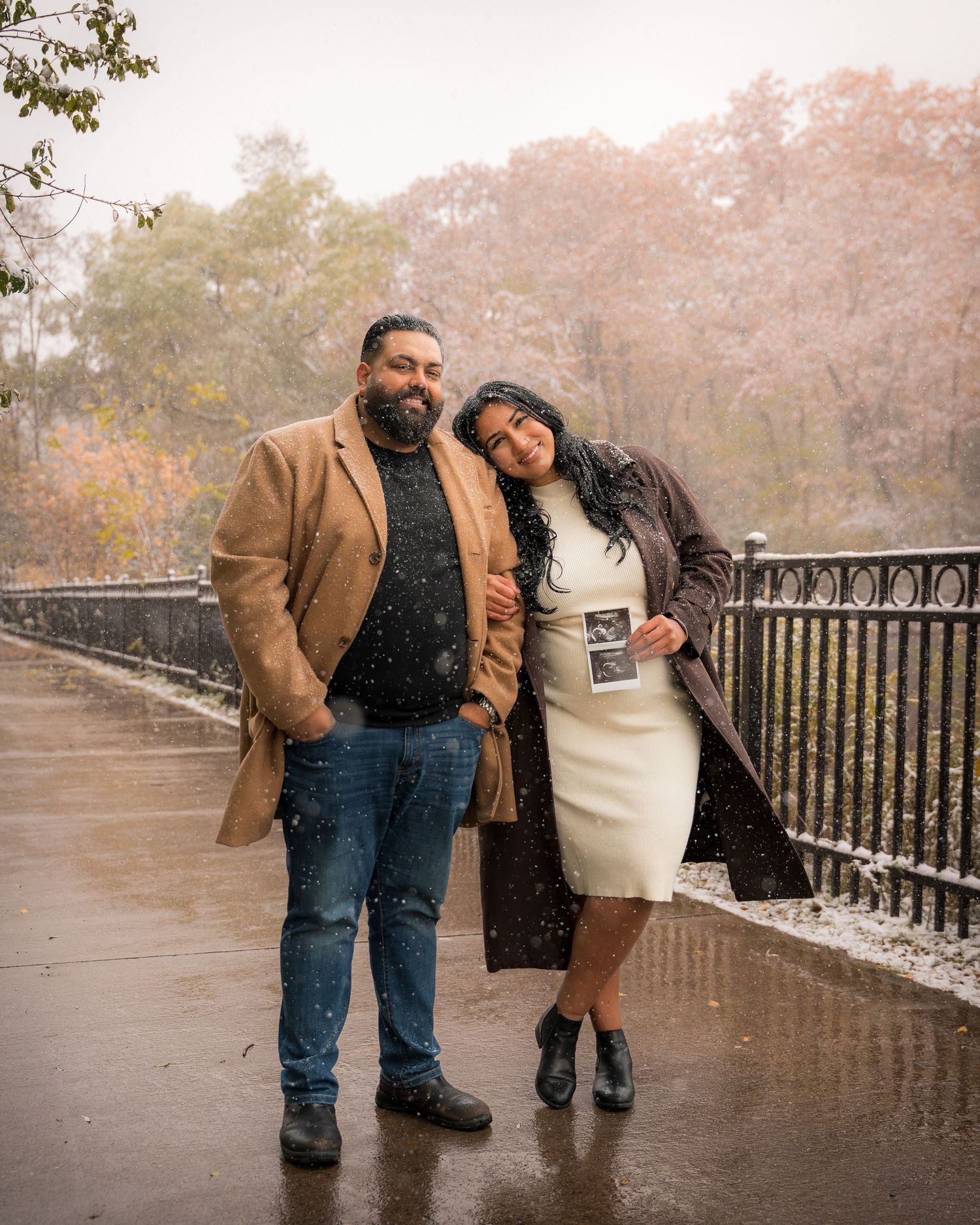 Romantic couple embracing on a misty bridge during autumn wearing coordinating brown and black outfits.