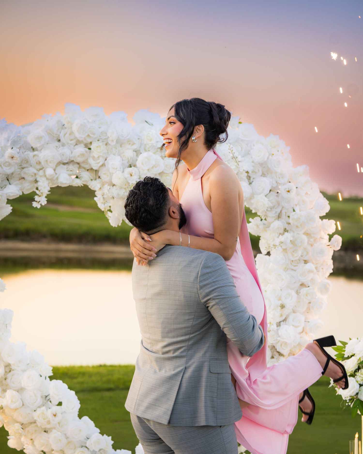 A tender embrace between newlyweds under an arch of white flowers during golden hour.