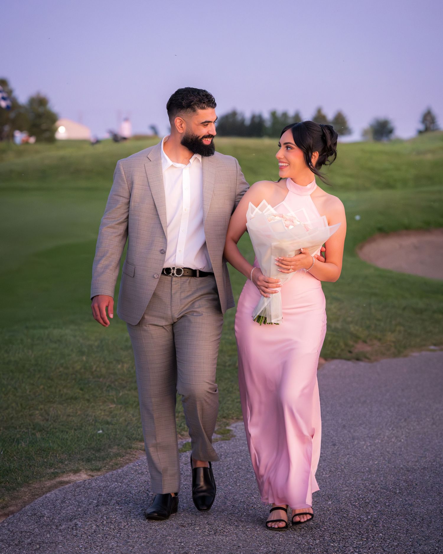 A couple takes a romantic stroll on a path while dressed in complementary pink and grey attire.