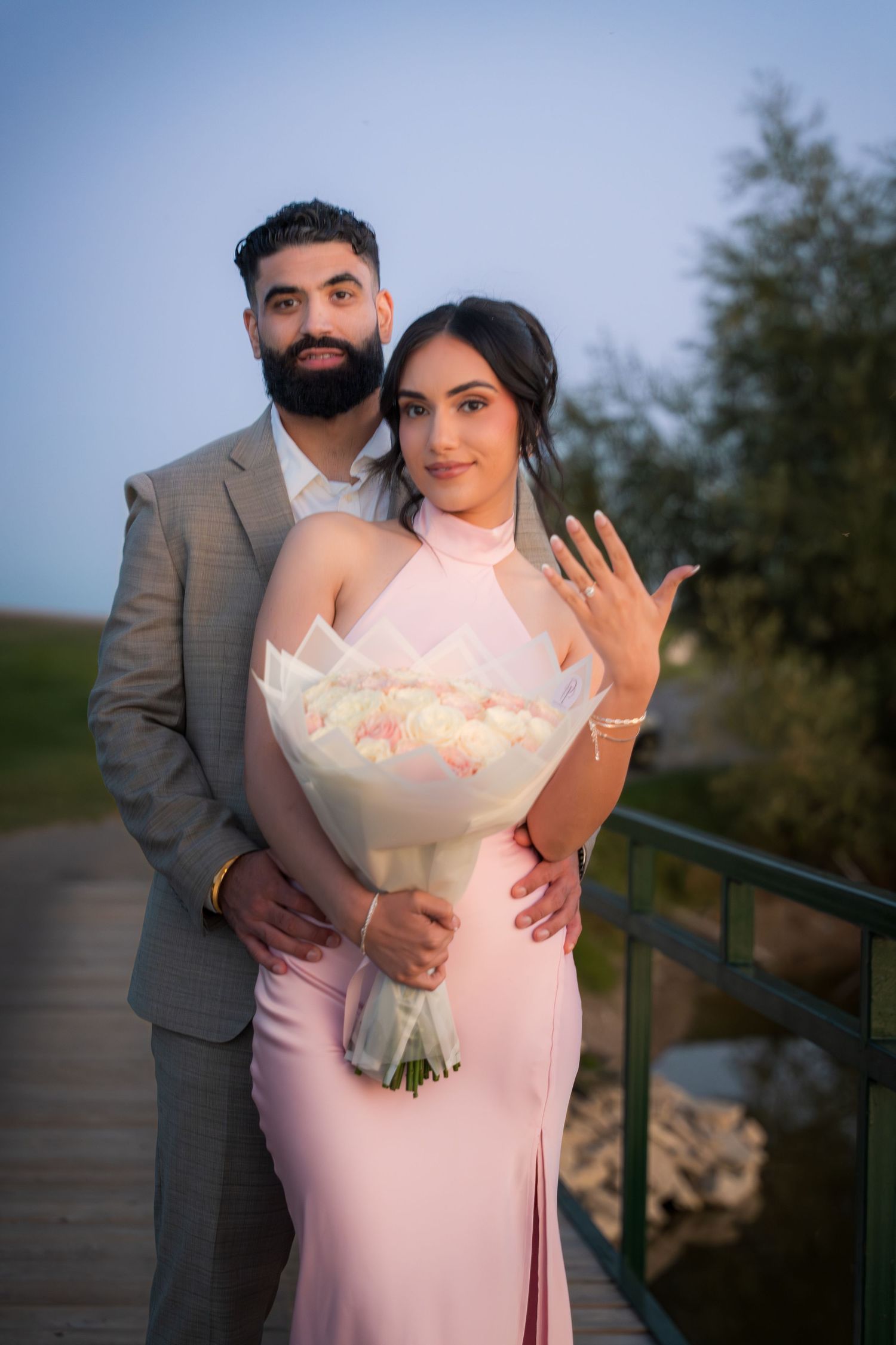 Couple shares romantic moment with white bouquet by lakeside railing.