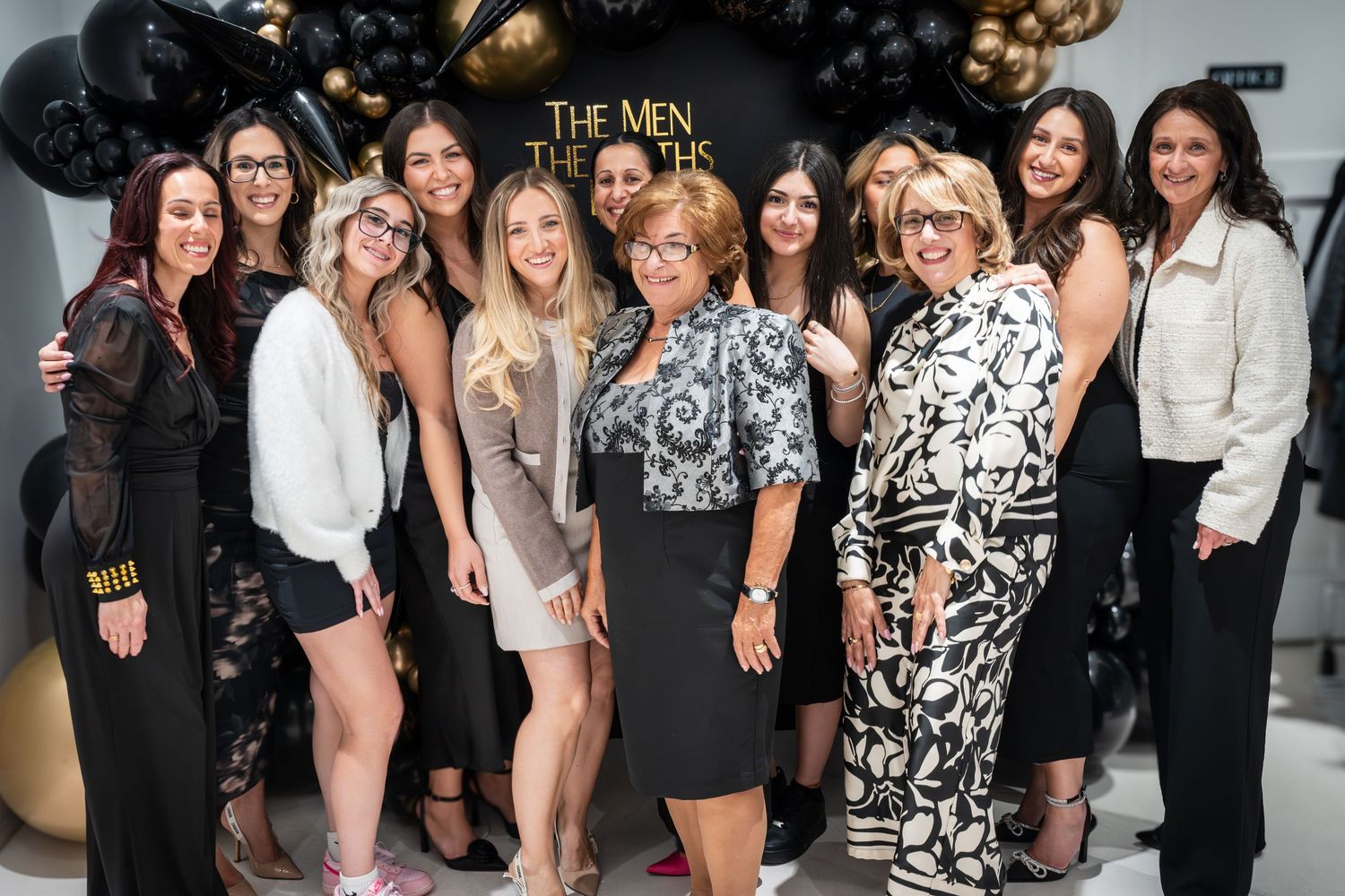 Group photo at a party with black and gold balloon decorations against a dark backdrop.