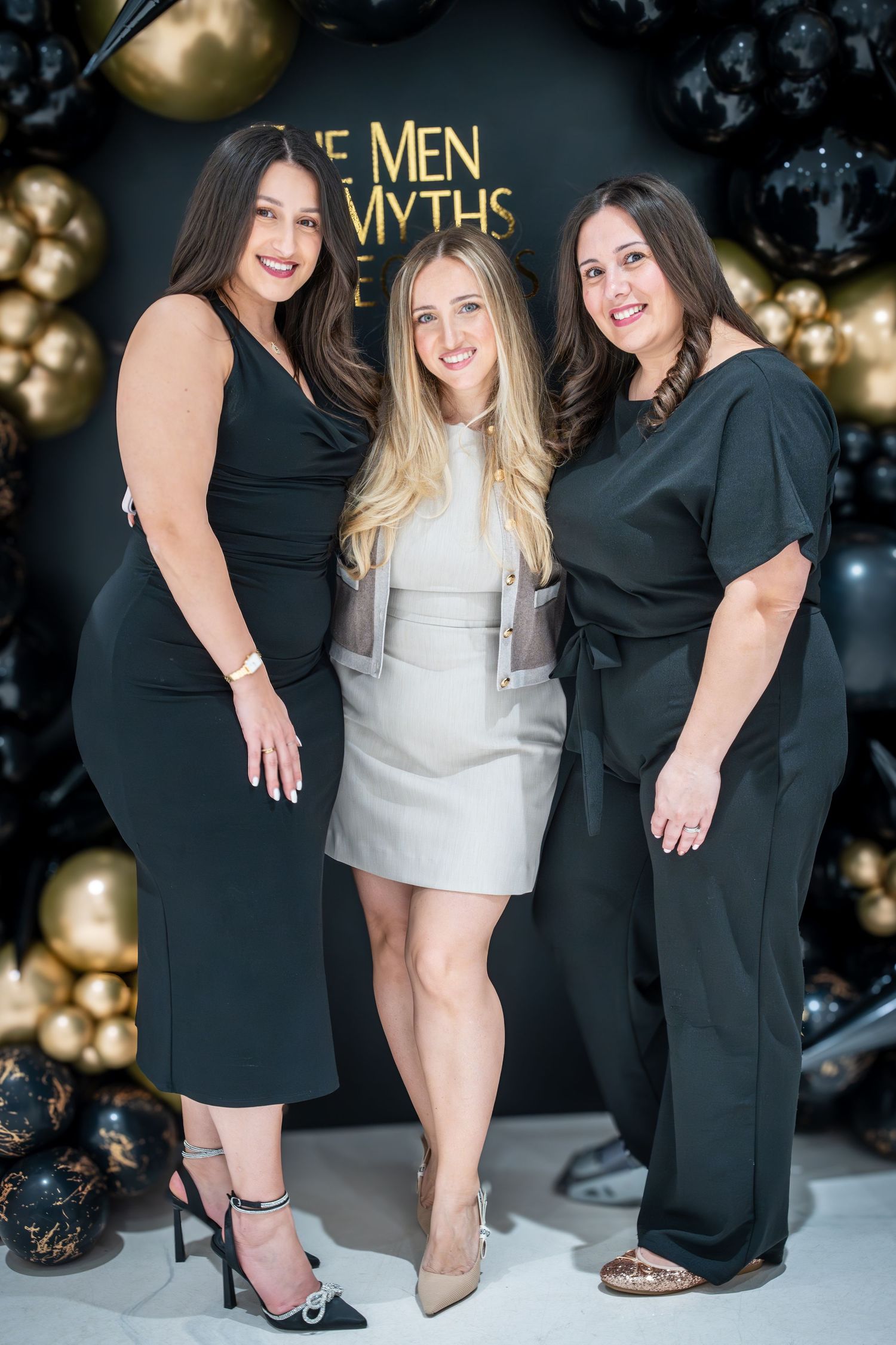 Three women in black and white dresses posing together at formal event.