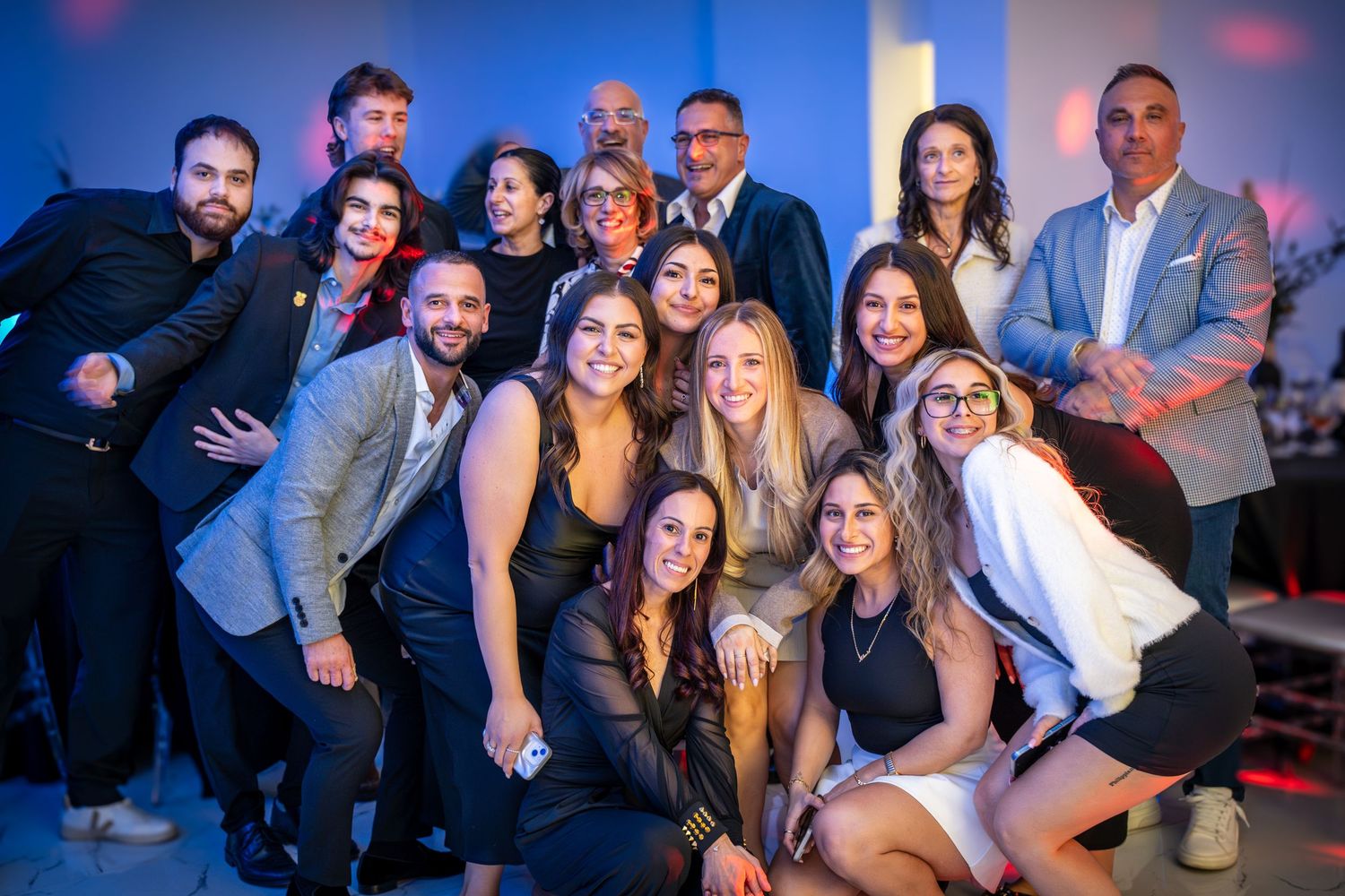 Group portrait of party guests posing together at celebratory event with blue lighting.