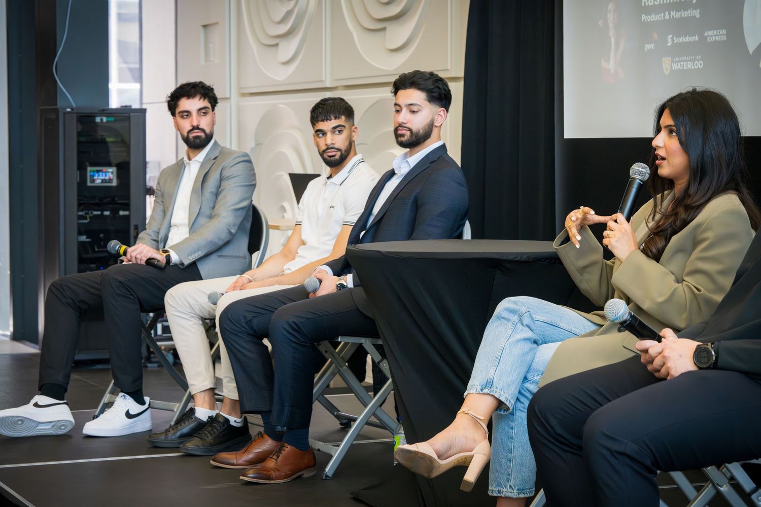 Side view of professional panel discussion with multiple speakers seated on folding chairs.