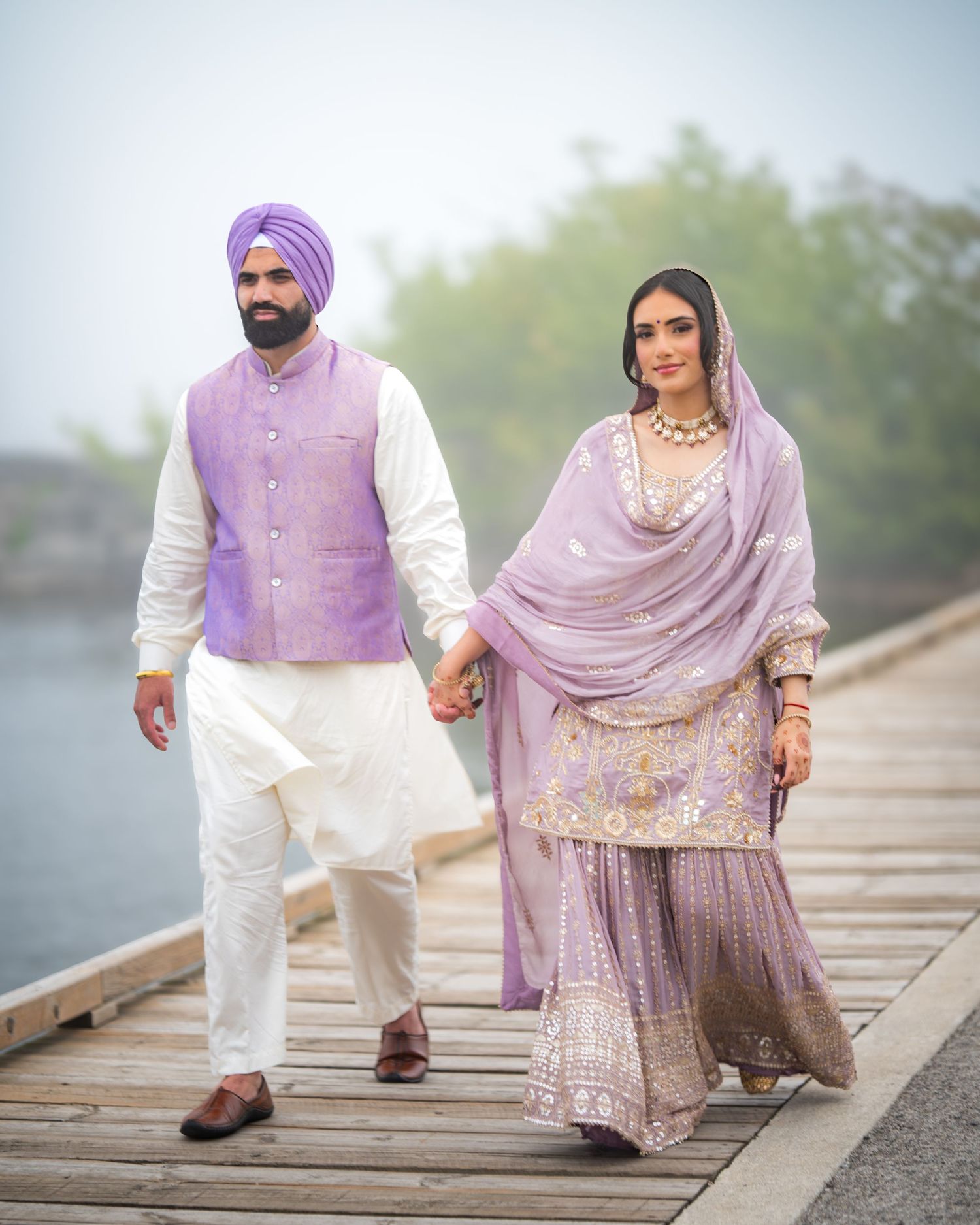 Couple holding hands while walking on a wooden path in coordinated purple and white outfits.