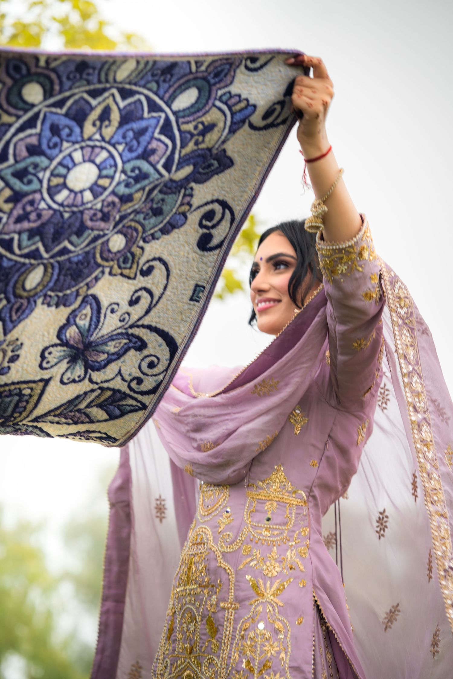 Beautiful embroidered lavender dupatta with intricate gold details being held up against a natural outdoor backdrop.