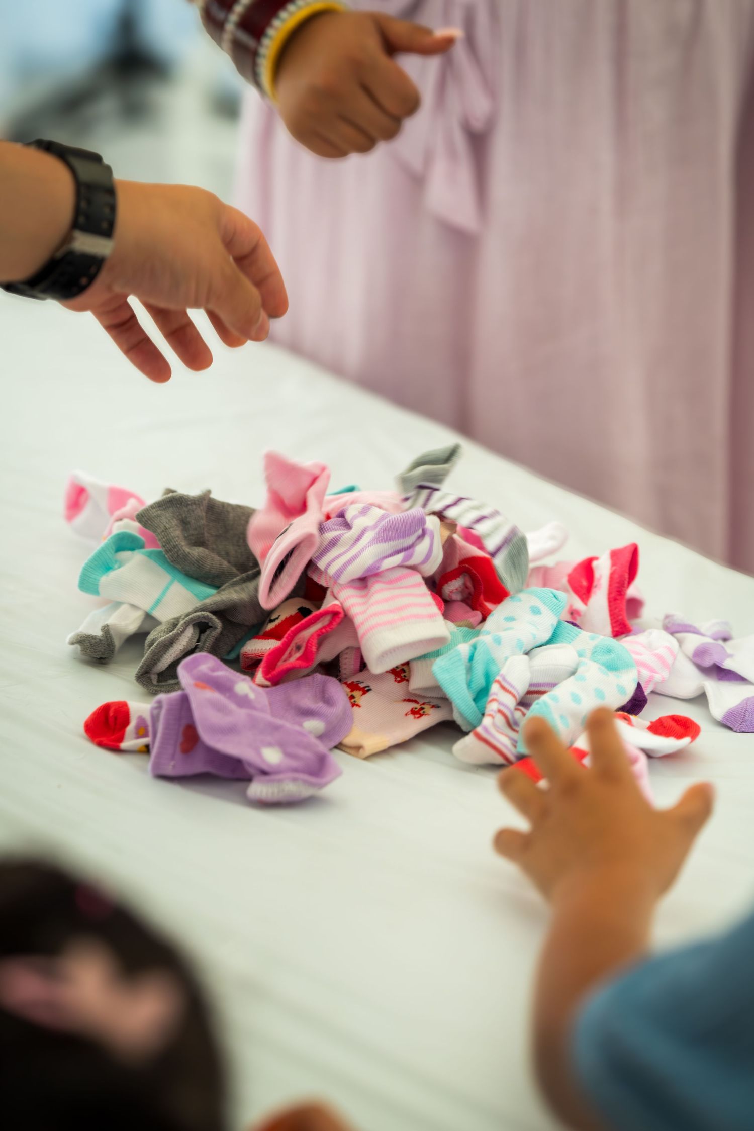 Hands working together to sort through colorful fabric pieces and ribbons on a white table.