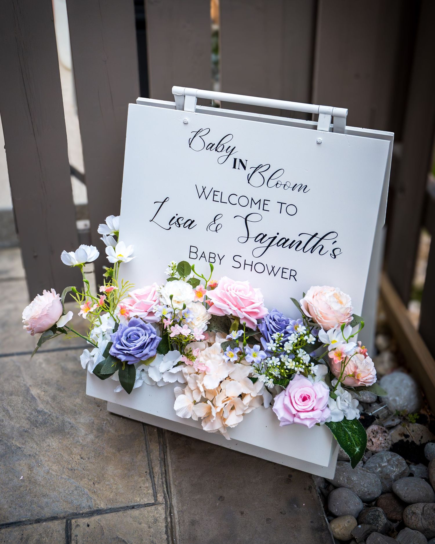 Elegant welcome sign decorated with pink and purple roses for a baby shower.