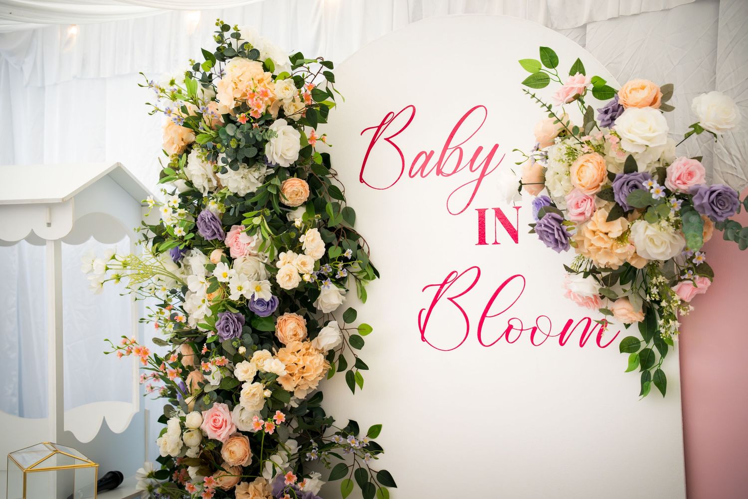 Elegant white and pink floral backdrop with 'Baby in Bloom' text for a special event.