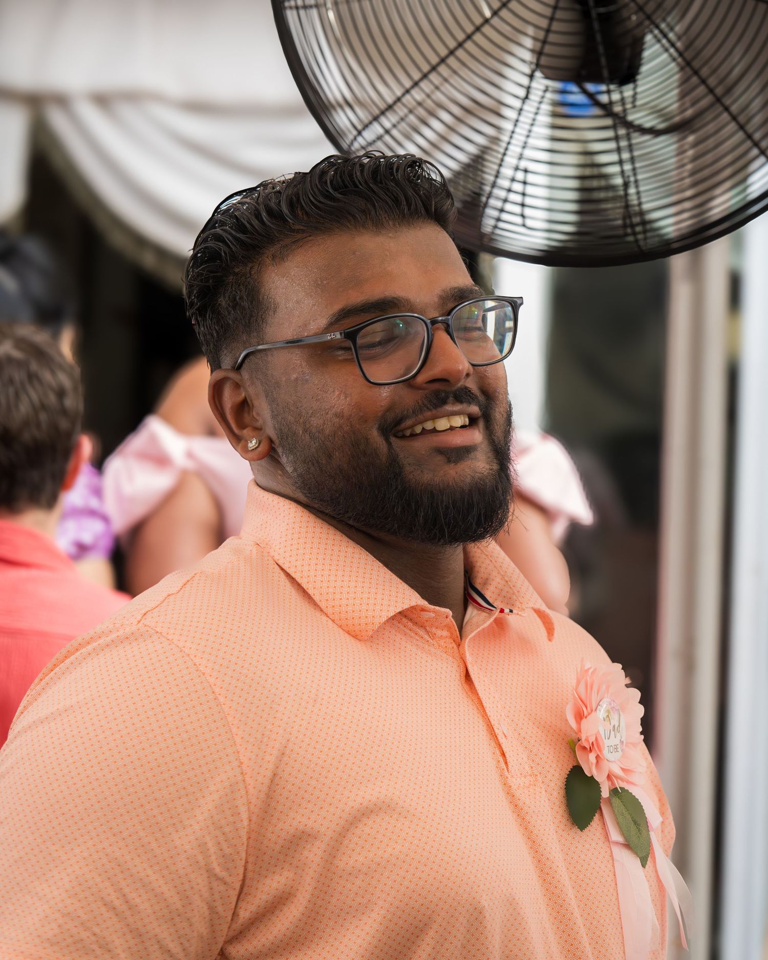 A person in a peach polo shirt smiles near a large fan at an outdoor event.