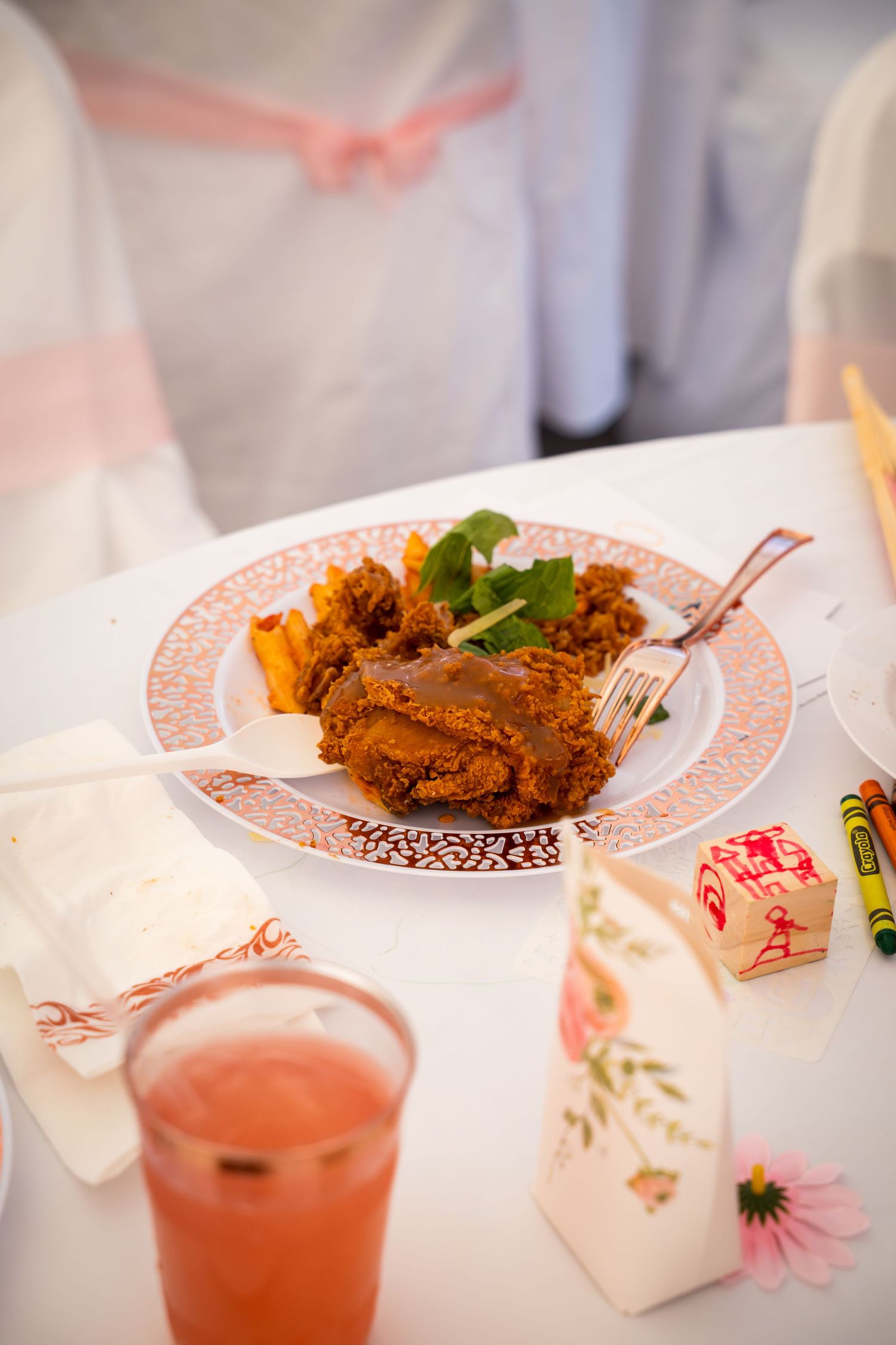 Plate of fried chicken with sides and a pink beverage on an elegant table setting.