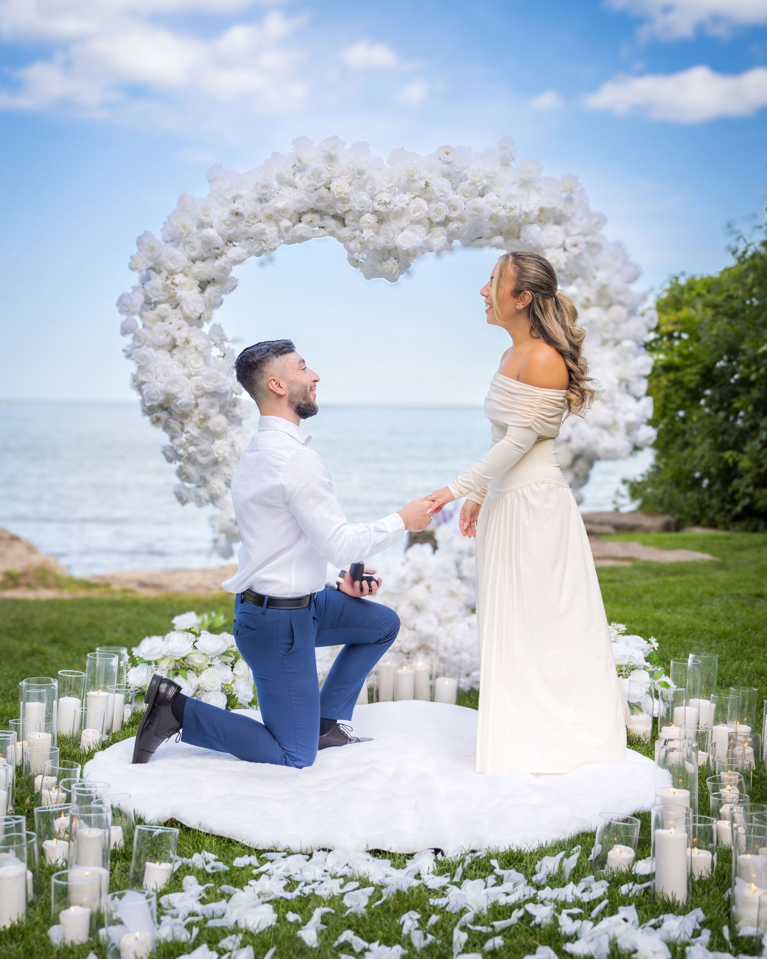 Romantic outdoor proposal with white floral decorations and candlelit path by the ocean.