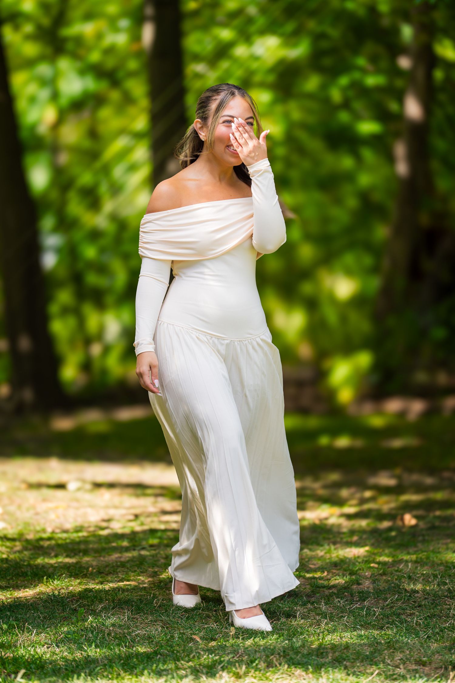 Bride in flowing white dress twirls in a sunlit forest setting.