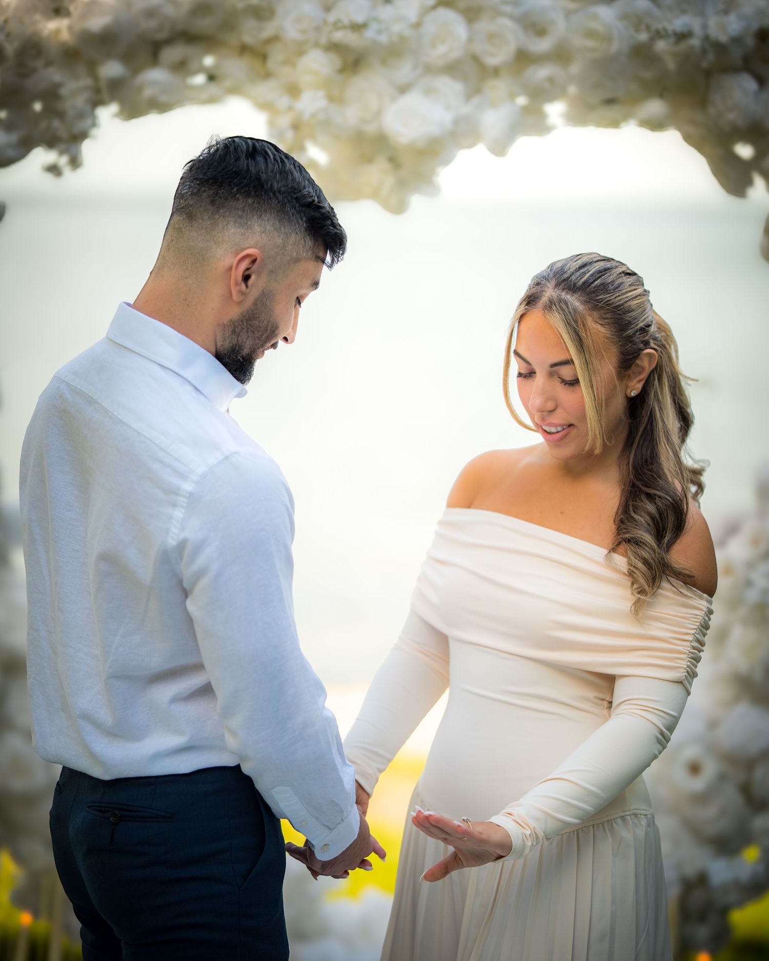 Elegant wedding couple dancing together under white floral decorations at an outdoor venue.