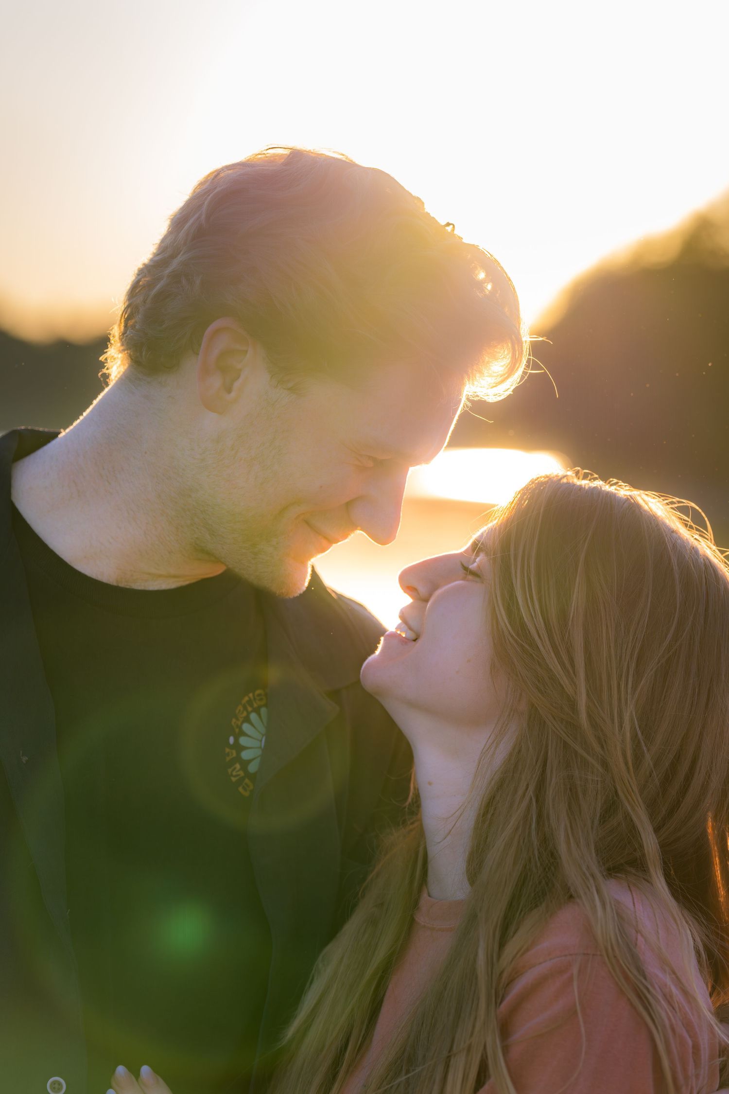 Romantic couple smiling and leaning in for a kiss bathed in warm golden sunset light.
